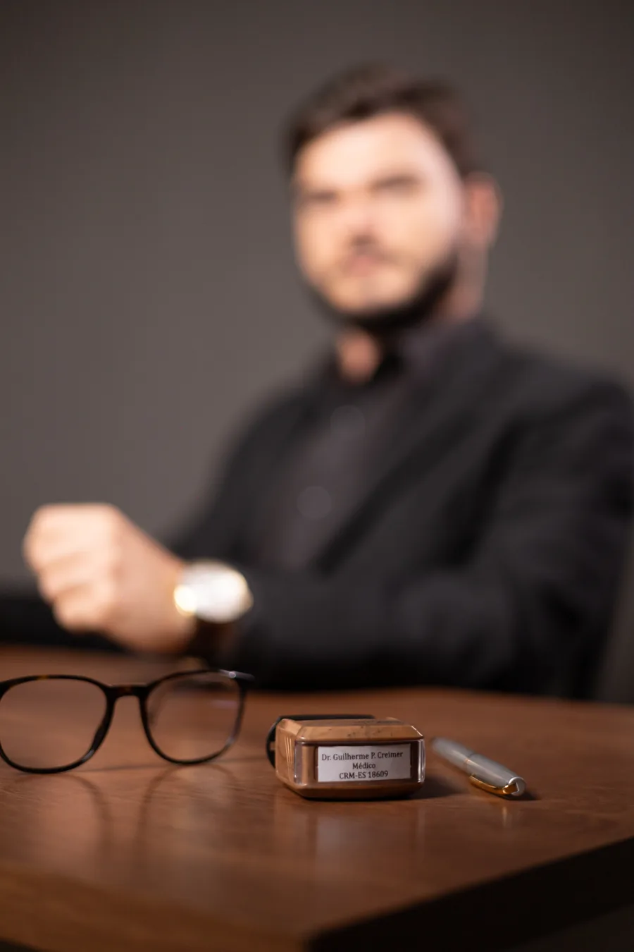 Carimbo profissional sobre a mesa, ao lado dos óculos e da caneta.